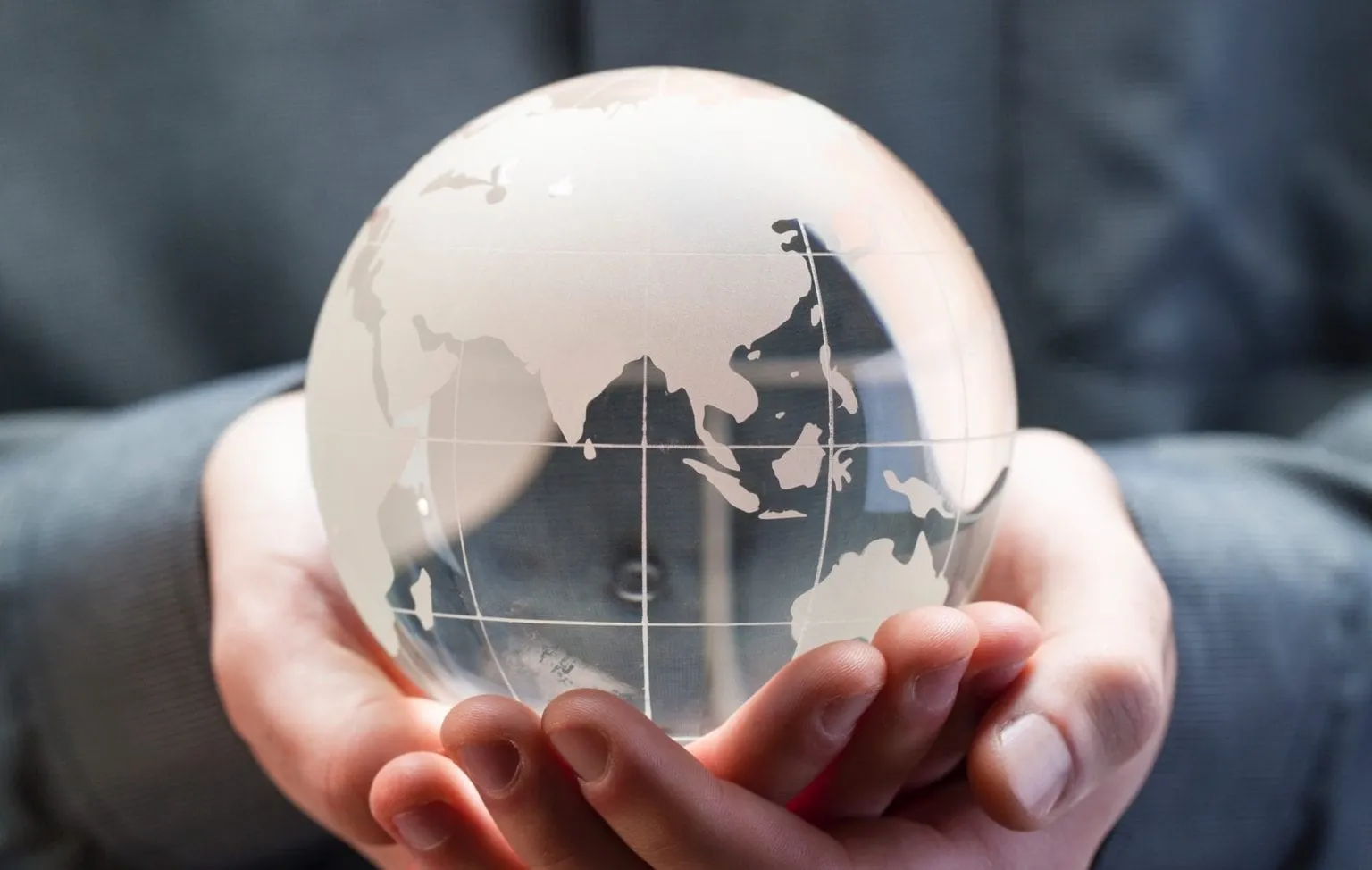 Hands hold a transparent globe showing the continents.