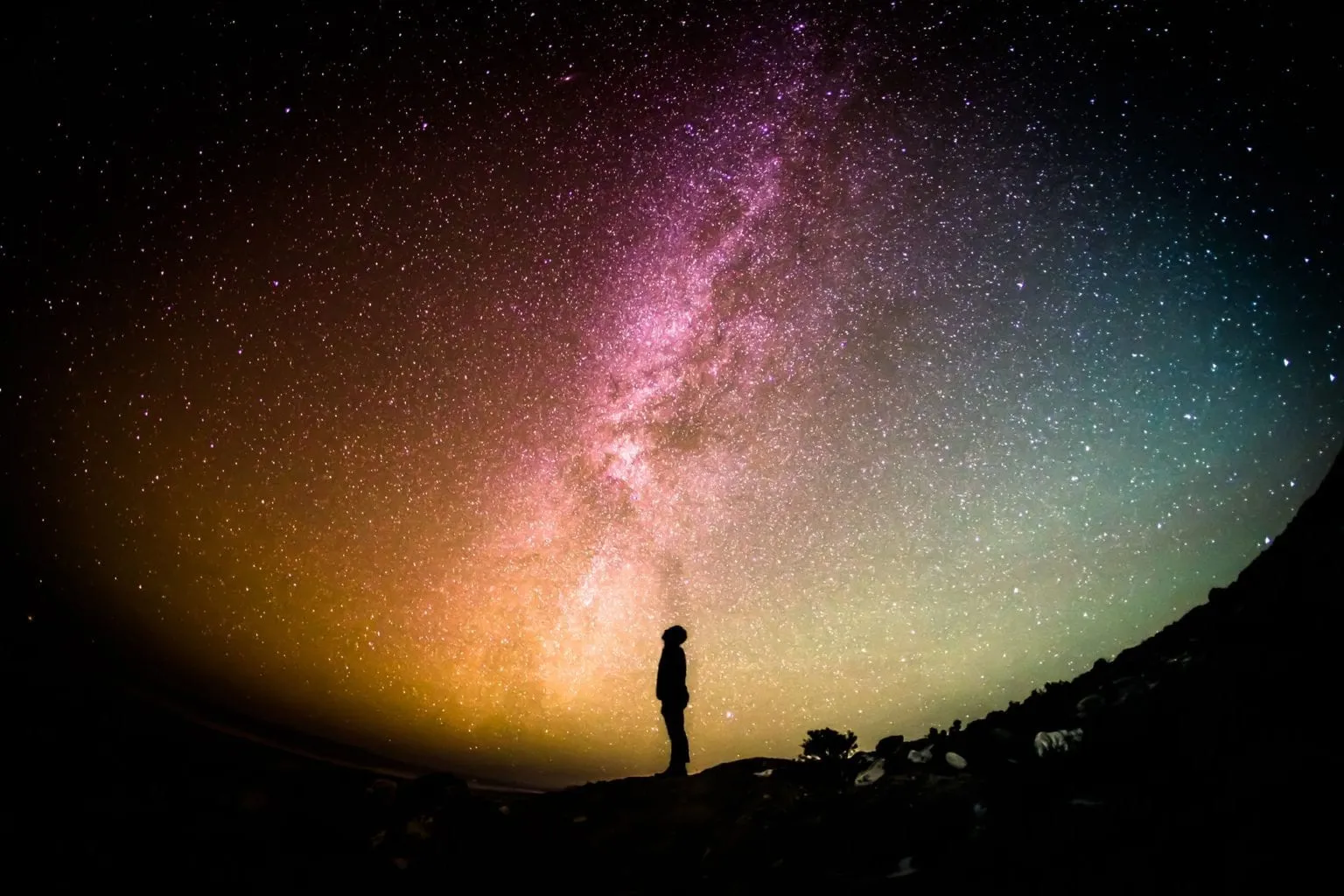 A person stands beneath the Milky Way in a star-filled sky.