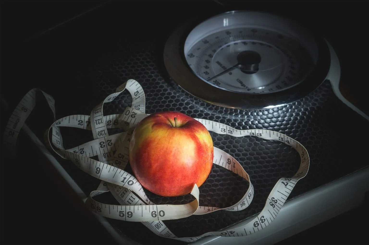 An apple and measuring tape rest on a bathroom scale.